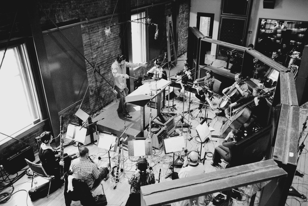 Wide, slightly overhead shot of composer, Jeff Toyne, conducting orchestra in recording studio.